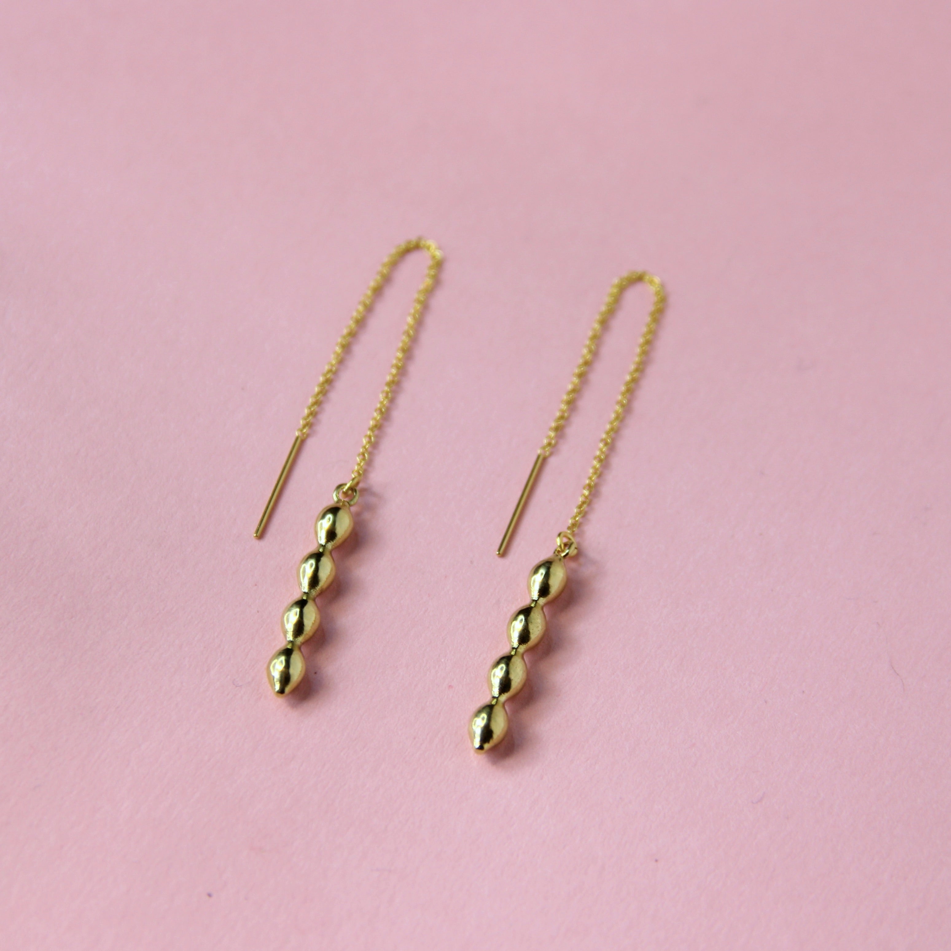 A gold toned threader earring with a bubble geometric charm