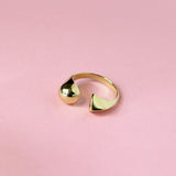 A gold-colored split shapes ring on a pink background