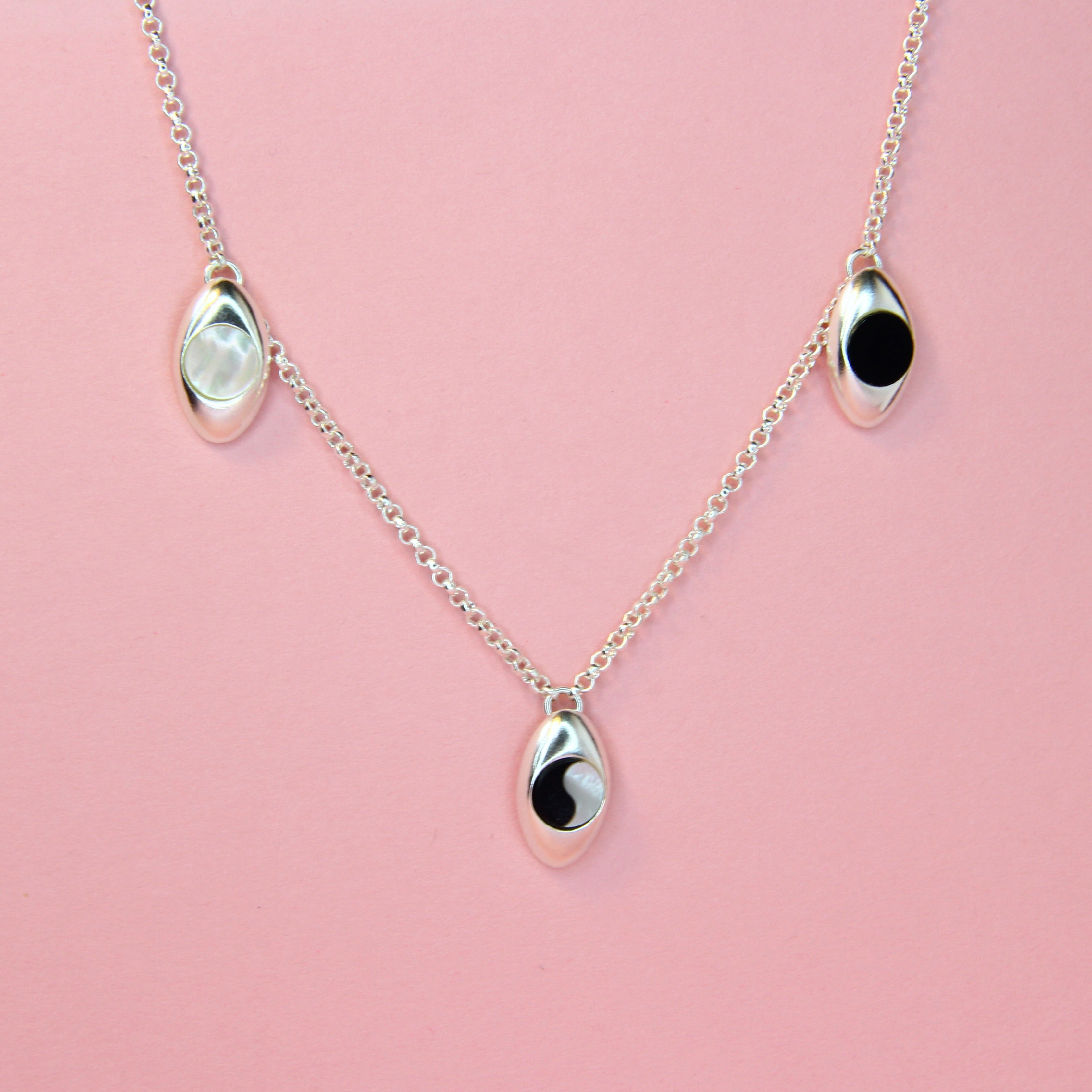 Silver charm necklace with oval pendants with mother of pearl, black onyx, and ying yang inlaid stones.