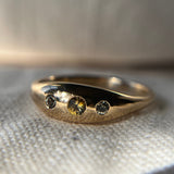 A hand-carved ring made of 14k yellow gold, featuring three kaleidoscope sapphires presented on a white surface.