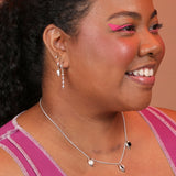 Person wearing stacked silver huggie hoops with geometric shaped charms