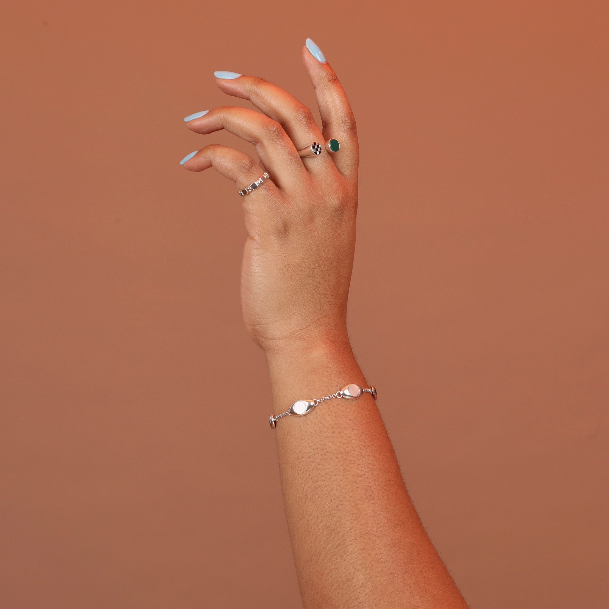 Woman wearing a silver charm bracelet featuring oval charms with mother of pearl stone inlay