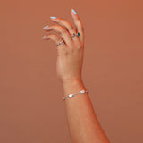 Woman wearing a silver charm bracelet featuring oval charms with mother of pearl stone inlay