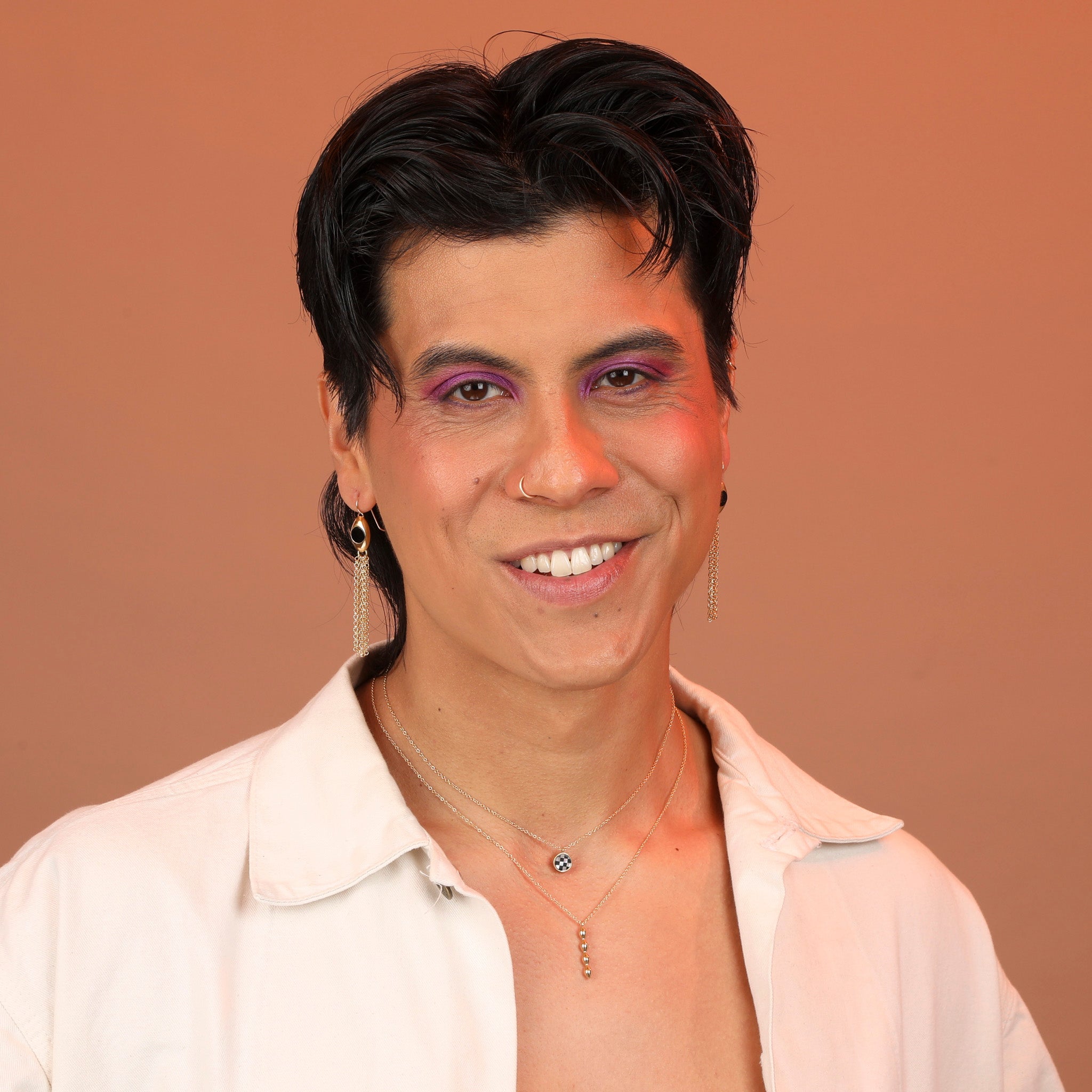 A person wearing two necklaces stacked together, one with a checkerboard pendant