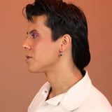 Person wearing a huggie hoop in bronze with a black onyx charm