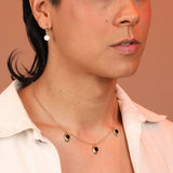 Person wearing a gold toned charm necklace with oval pendants and black onyx stones.