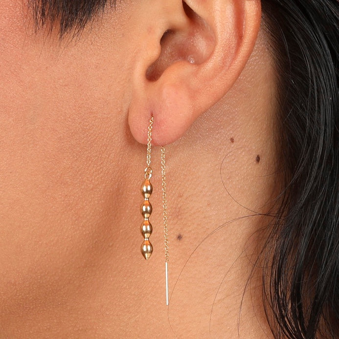 A close-up image of a person wearing a gold-colored bubble charm threader earring.