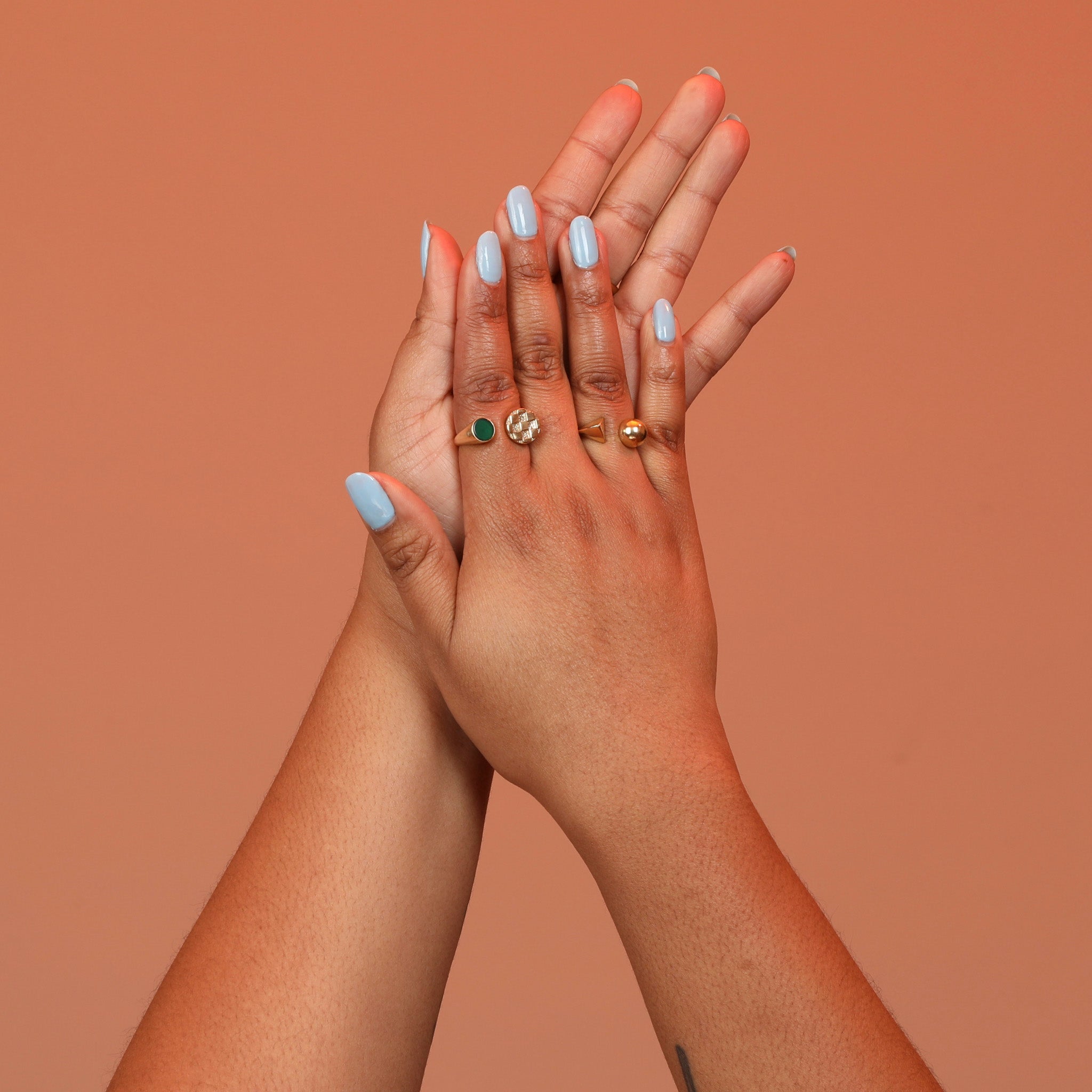 A hand wearing two split shank rings, one with a checkerboard metal pattern on one side and a green chrysoprase inlay stone on the other