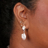 Person wearing earrings that feature a silver oval post with mother of pearl inlay and a baroque pearl dangling below