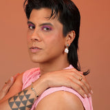 Person wearing a bronze pair of earrings with an oval post with checkerboard inlay and a dangling pearl