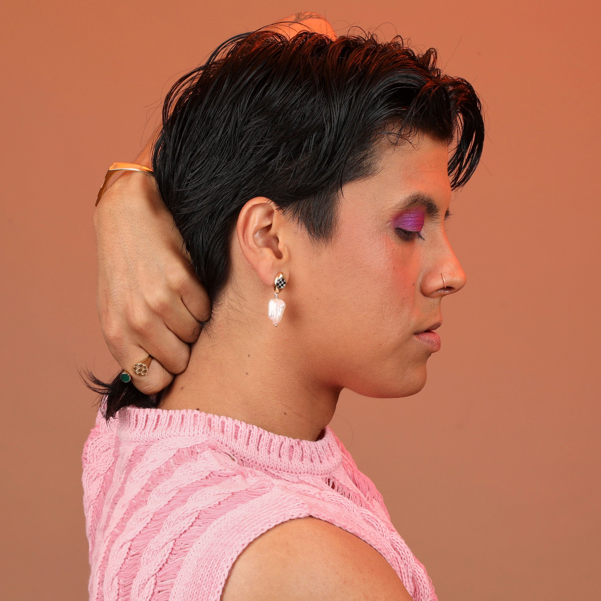 Person wearing bronze dangle earrings with an oval post with checkerboard inlay and a pearl dangling below