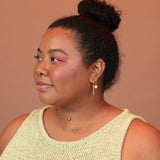 Woman wearing a layered ear stack of gold colored huggie hoops featuring a charm with mother of pearl and a separate charm of a geometric shape