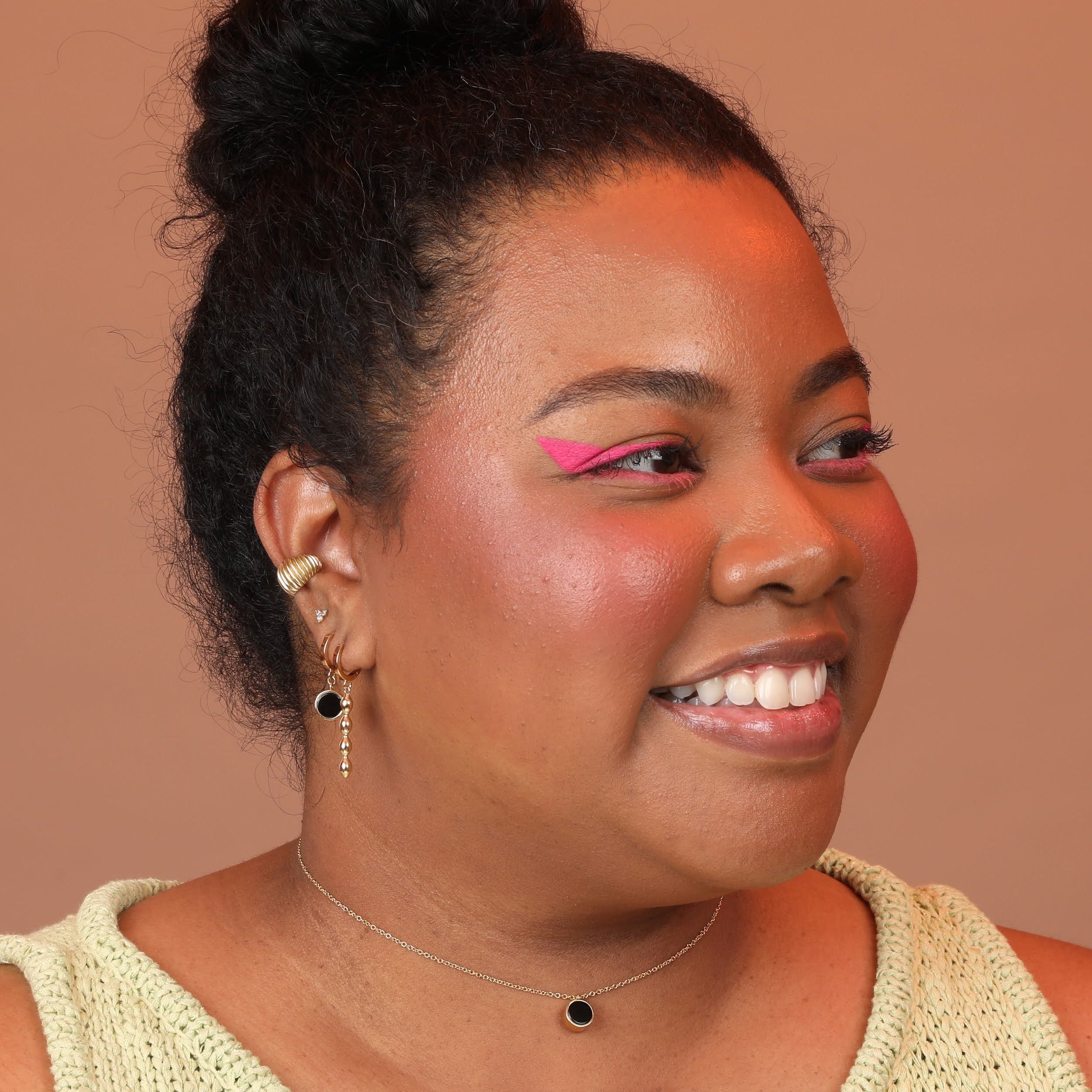 Woman wearing a layered ear stack of huggie hoops and a ribbed ear cuff in gold