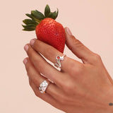 Close up of a person wearing silver rings with white mother of pearl stones, holding a strawberry