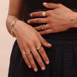 A person wearing a variety of gold colored bronze jewelry in geometric styles