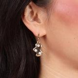 A close-up of a person's face focusing on the earrings, which are colorful and fun, with bronze gold and mother of pearl being prominent colors.