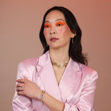 A person wearing a pink top and a gold-colored geometric necklace and bracelet with a spiral pattern