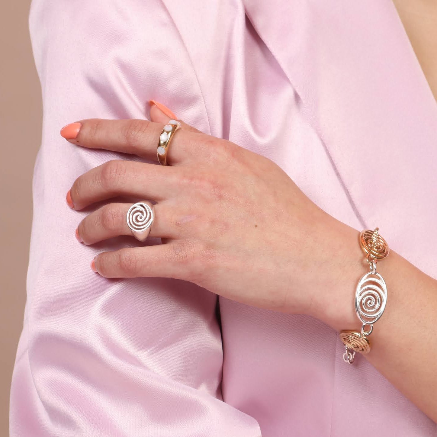 Person wearing an assortment of jewelry including a gold toned band with white mother of pearl stones, a silver spiral signet and a mixed metal spiral bracelet