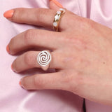 A hand wearing a silver spiral signet ring on a pink satin surface.