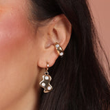 A woman wearing a cloud shaped huggie hoop earring and an ear cuff, both gold toned bronze with mother of pearl stones