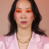 A person wearing a pink jacket and a gold paperclip chain necklace with two hooks on the ends.
