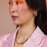 A person wearing a pink blazer, brass paperclip chain necklace and spiral earrings