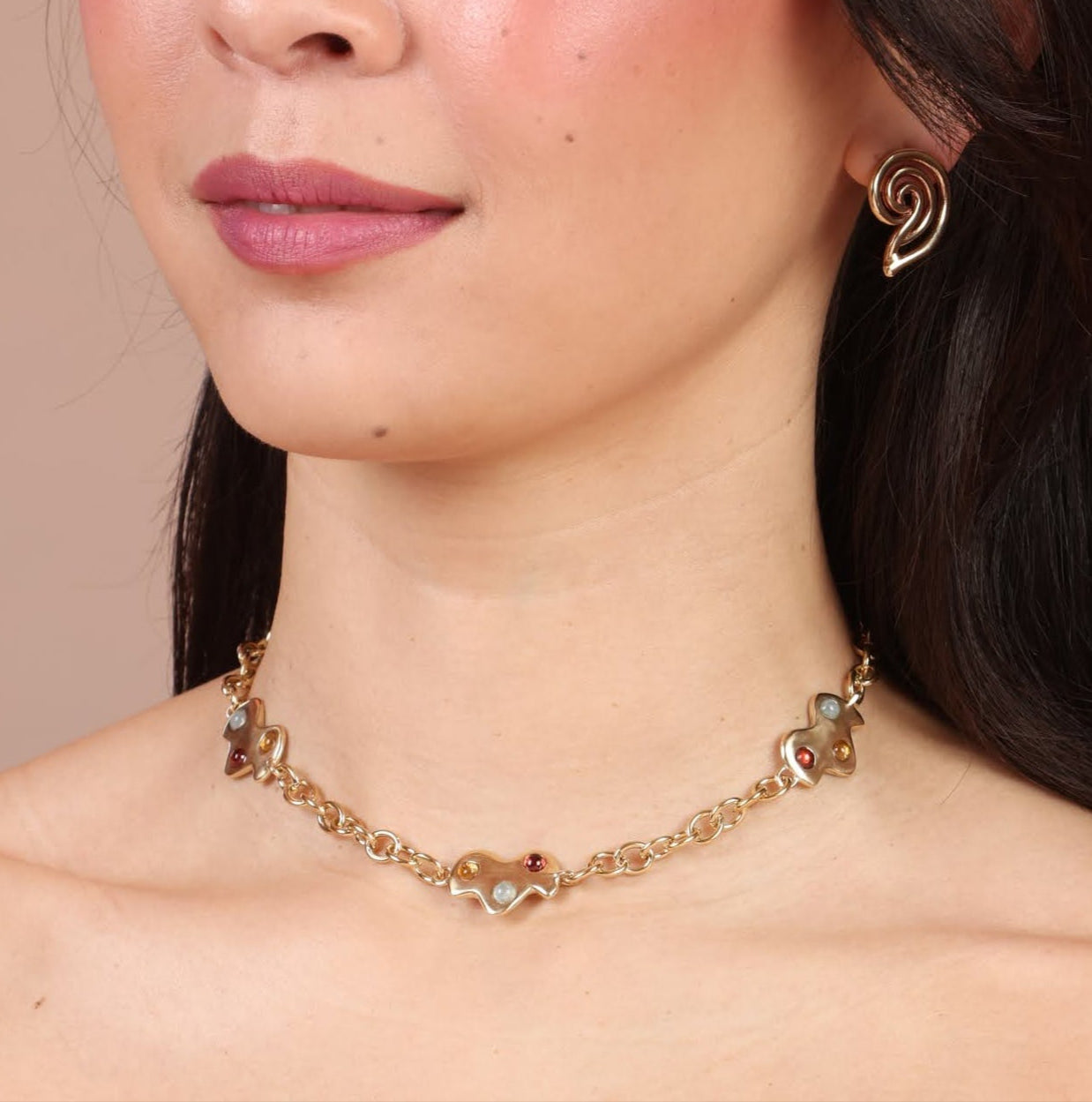 A person wearing a gold-colored necklace with three charms shaped like clouds, displayed against a neutral background.