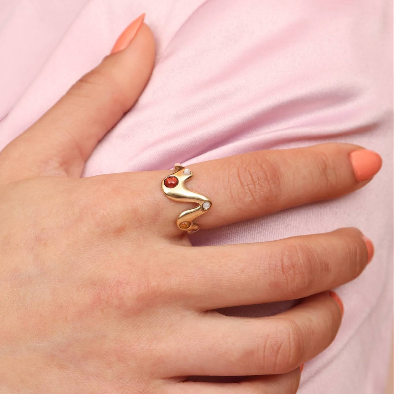 Person wearing a gold toned bronze wavy ring with red garnet, yellow citrine, and mother of pearl cabochon inlay stones