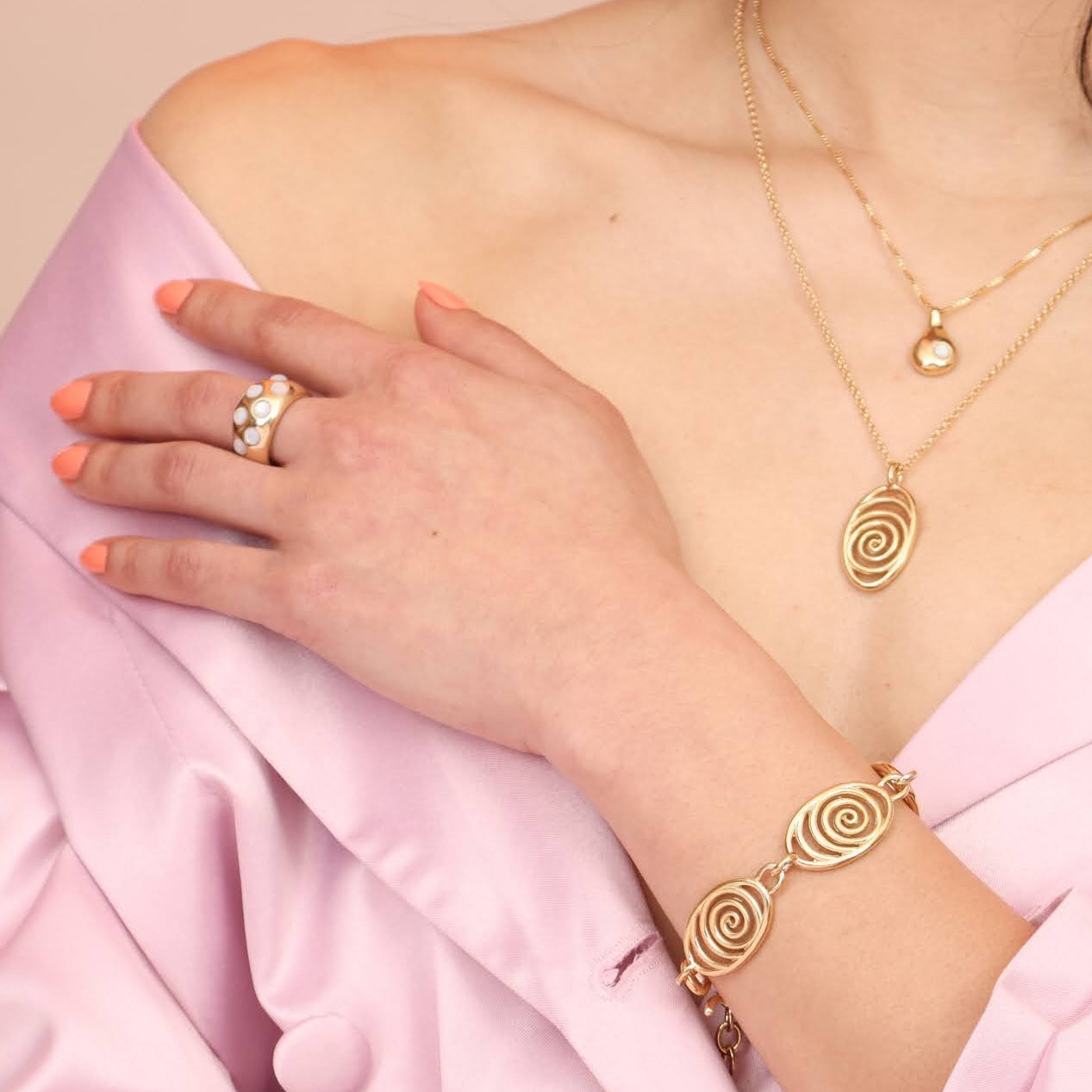 Person wearing an array of gold colored jewelry including a spiral pendant and bracelet, and a thick gold ring with mother of pearl stones