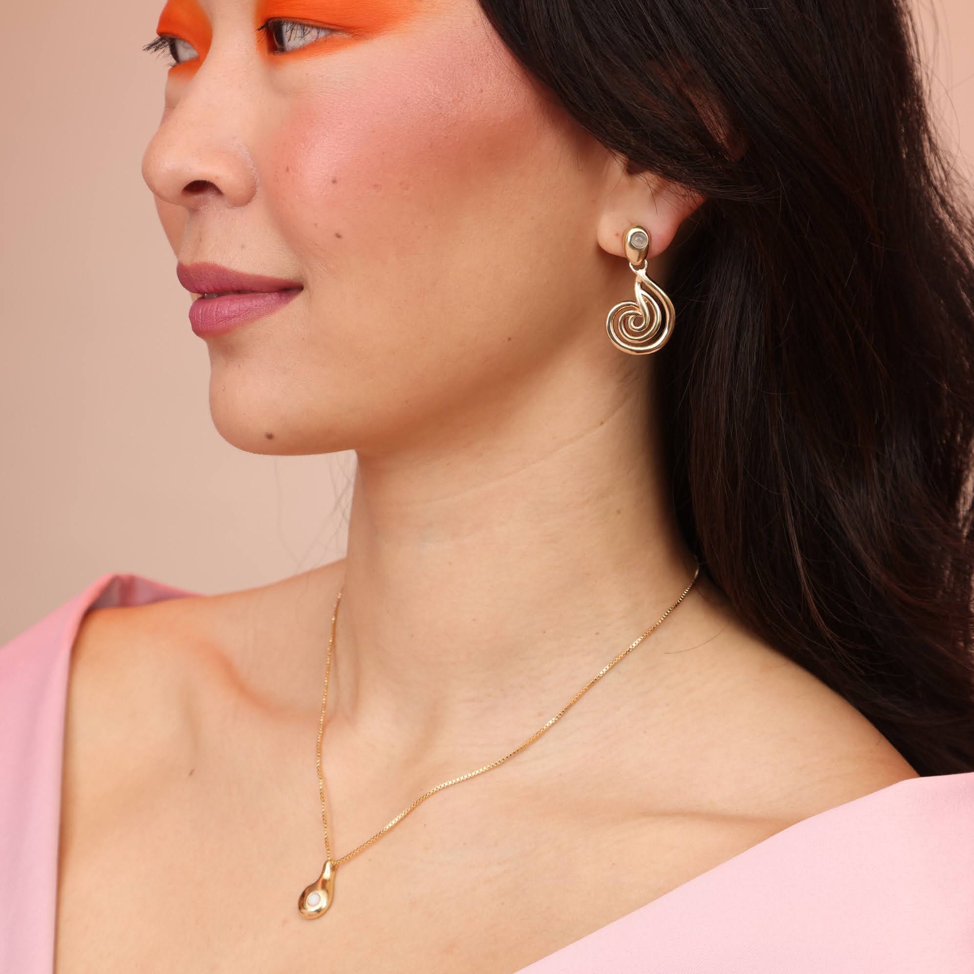 A person wearing a gold teardrop necklace with spiral earrings
