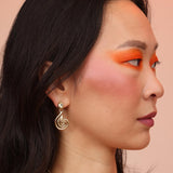 A side profile of a person wearing gold-colored spiral-shaped dangle earrings with a blue aquamarine stone