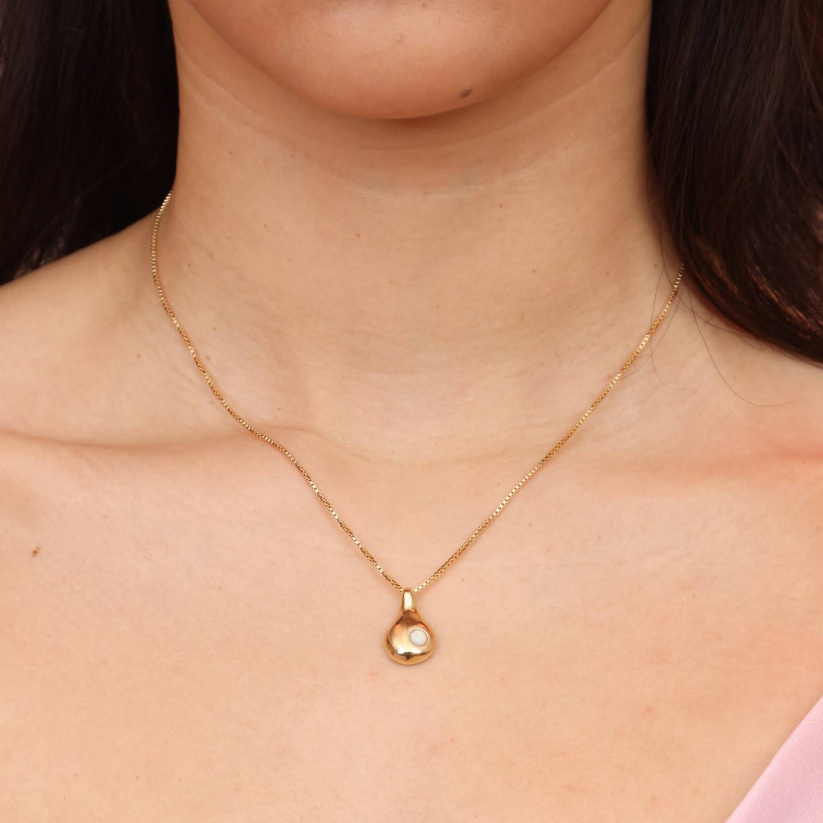 A person wearing a gold colored bronze teardrop shaped necklace with an opal stone
