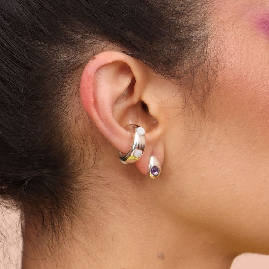 A woman wearing a silver ear cuff with white mother of pearl stones and a small silver teardrop earring with a purple amethyst stone