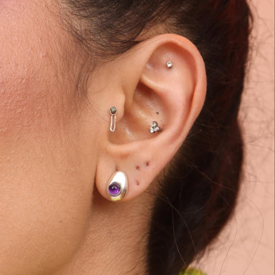 A side profile of a person wearing a teardrop-shaped earring with a purple amethyst stone.