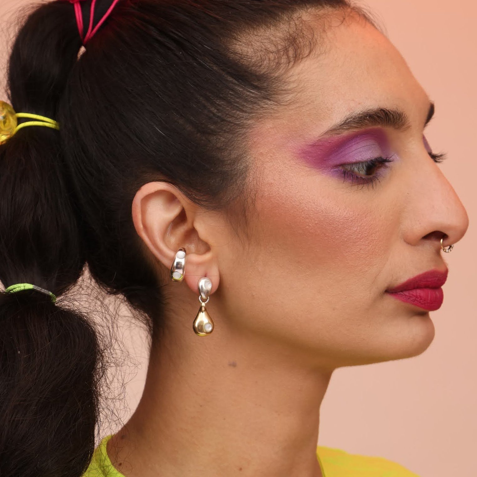 A woman wearing silver and bronze dangle earrings with a geometric drop design.