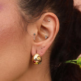 A person wearing gold-colored hoop earrings with gemstones.