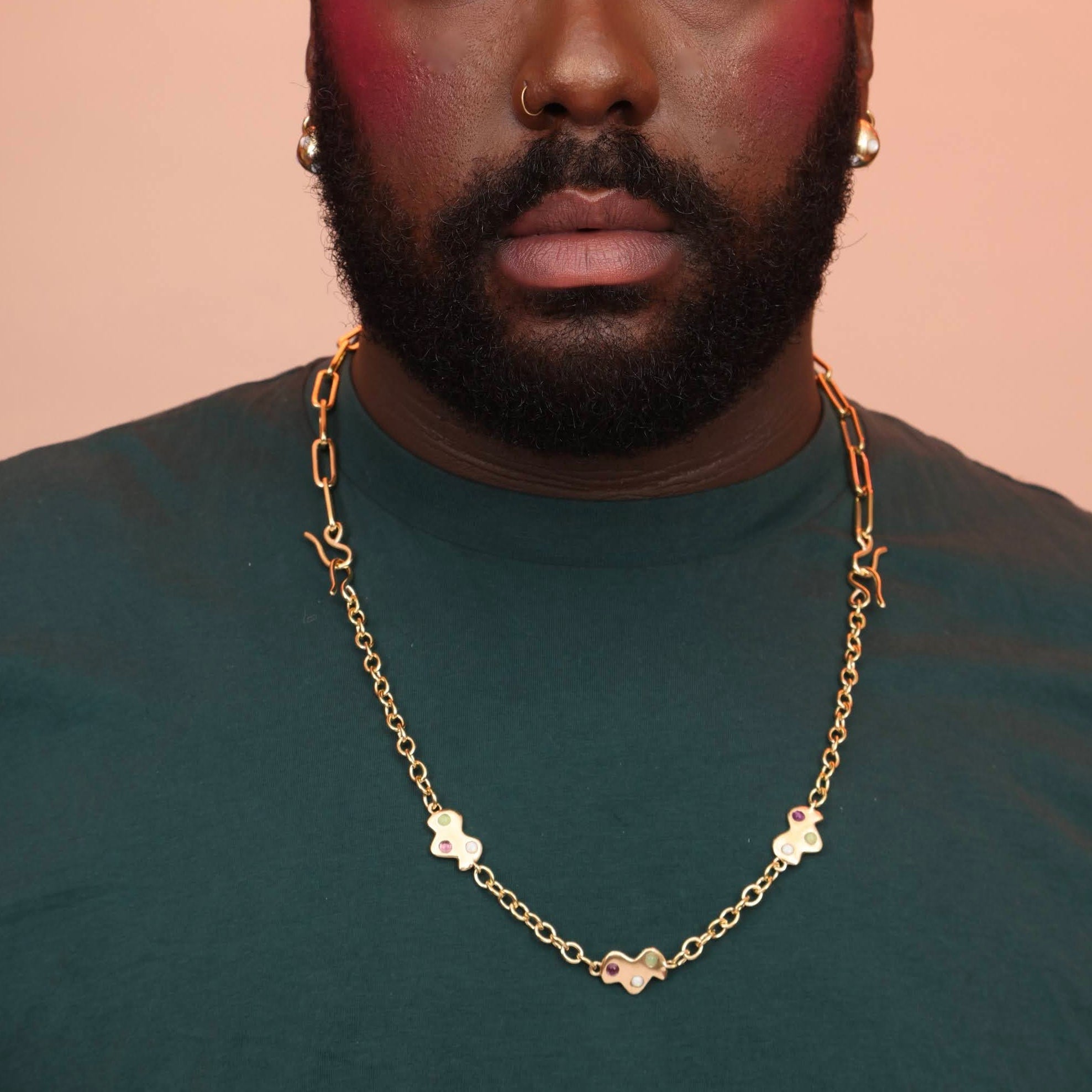 A man wearing a long gold necklace with cloud charms and red, blue, and yellow stones