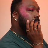 Man with gold jewelry and pink makeup on a peach background