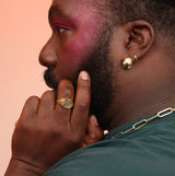 A person wearing a bronze spiral ring and a bubble hoop with white stones