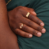 A hand wearing a bronze signet with a red and white stone and another bronze checkerboard signet ring