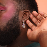 A close-up of a person's face focusing on the earrings, which are silver cloud shaped huggies featuring purple, teal, and opal stones