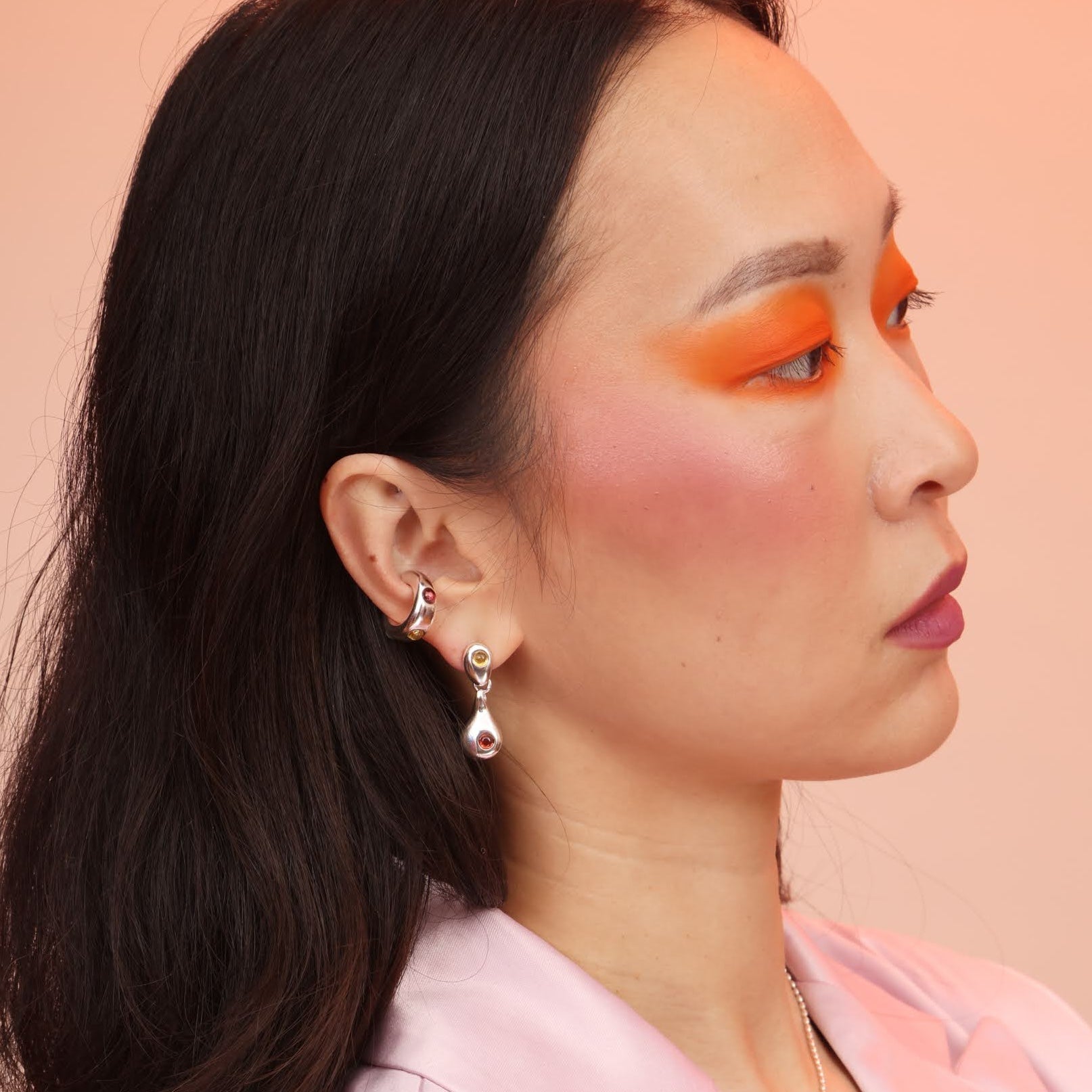 Woman wearing silver droplet earrings with garnet and citrine, as well as a silver ear cuff with stones
