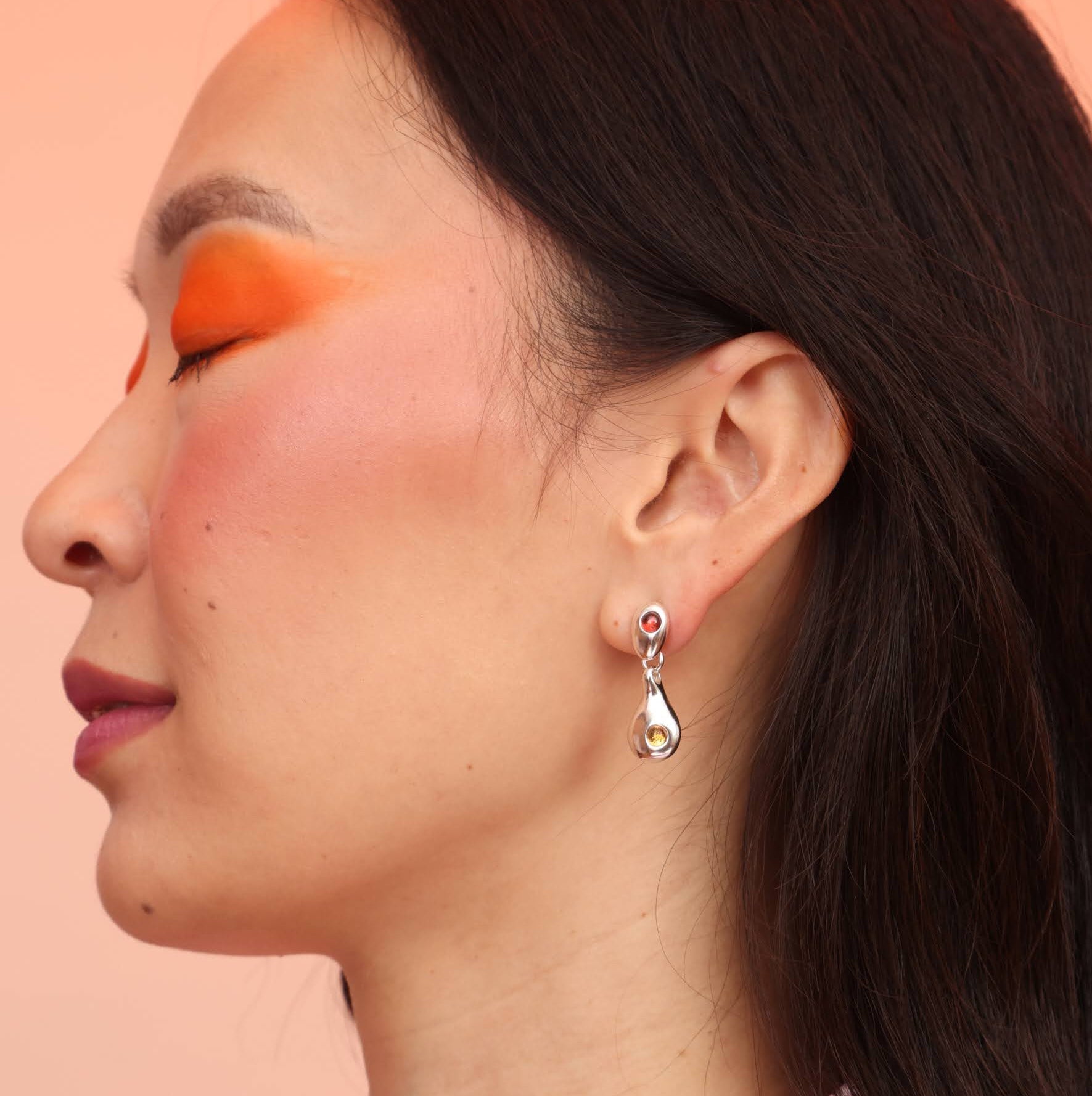 A close-up image of a woman's ear wearing a silver-colored drop-shaped dangle earring.