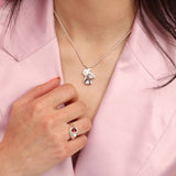 A silver cloud pendant on a ball chain necklace next to a hand wearing a silver signet with a red teardrop and pearl circle stone.