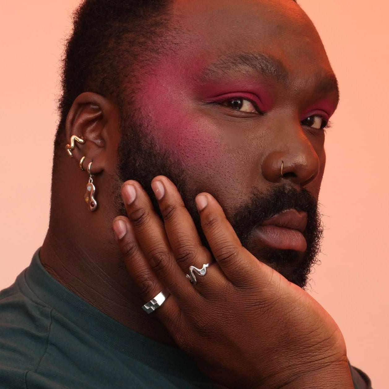 Person wearing an assortment of jewelry including a wavy ring, a checkerboard signet, cloud shaped earrings and a wavy ear cuff