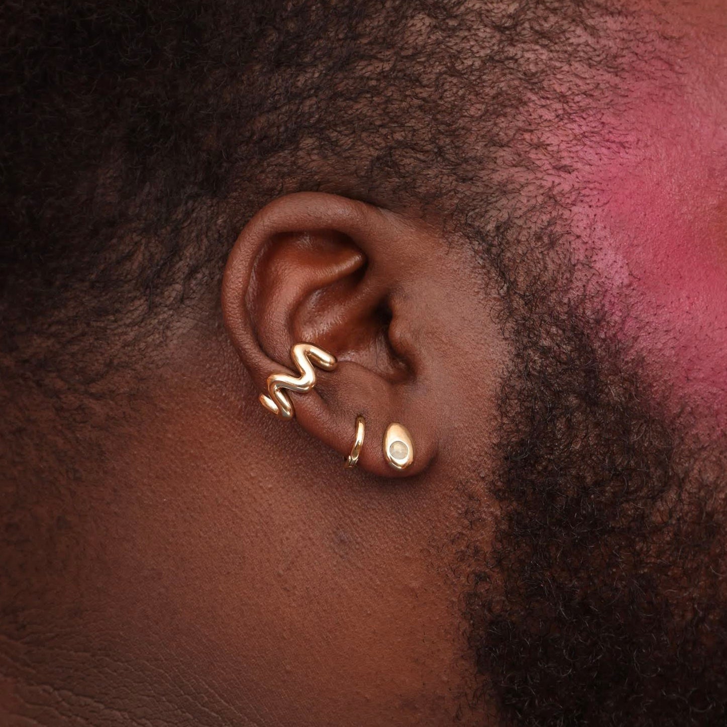 A side profile of a person wearing a bronze teardrop-shaped earring with a blue stone accent, as well as a bronze squiggly ear cuff