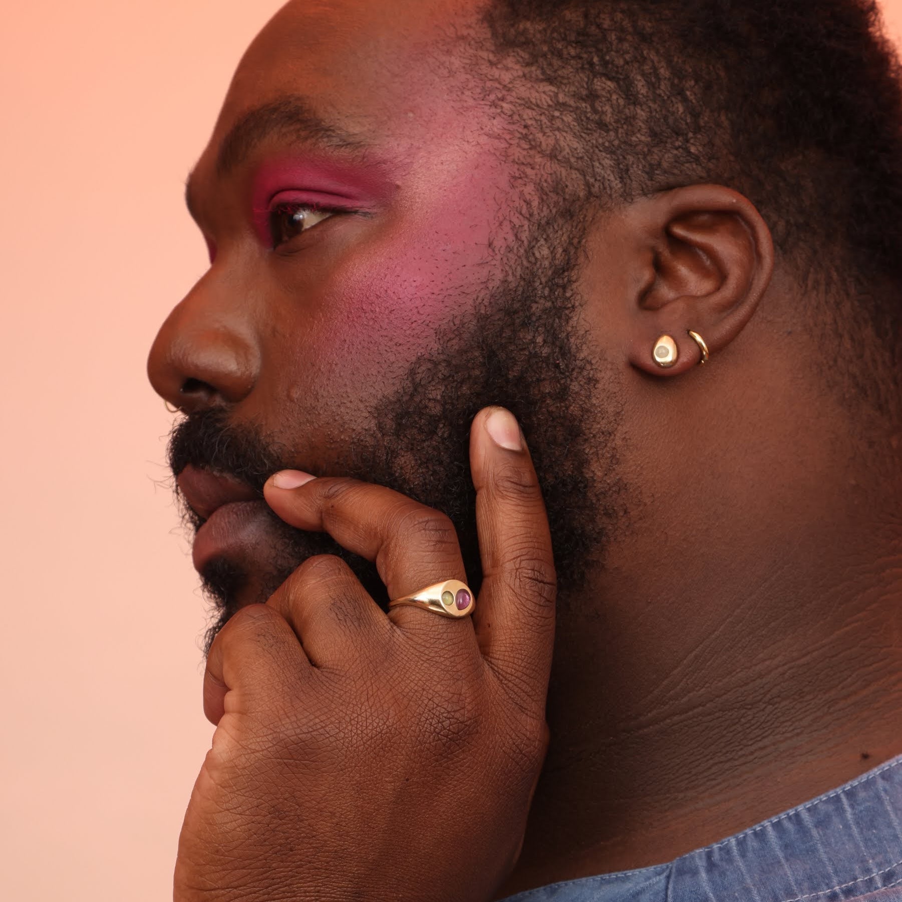 A side view of a person wearing a bronze teardrop post earring with a blue stone and a bronze signet ring