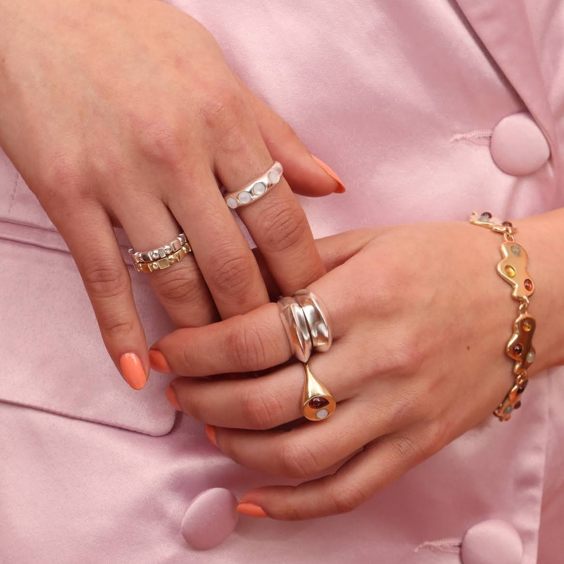 Person wearing bronze and silver rings with a pink background