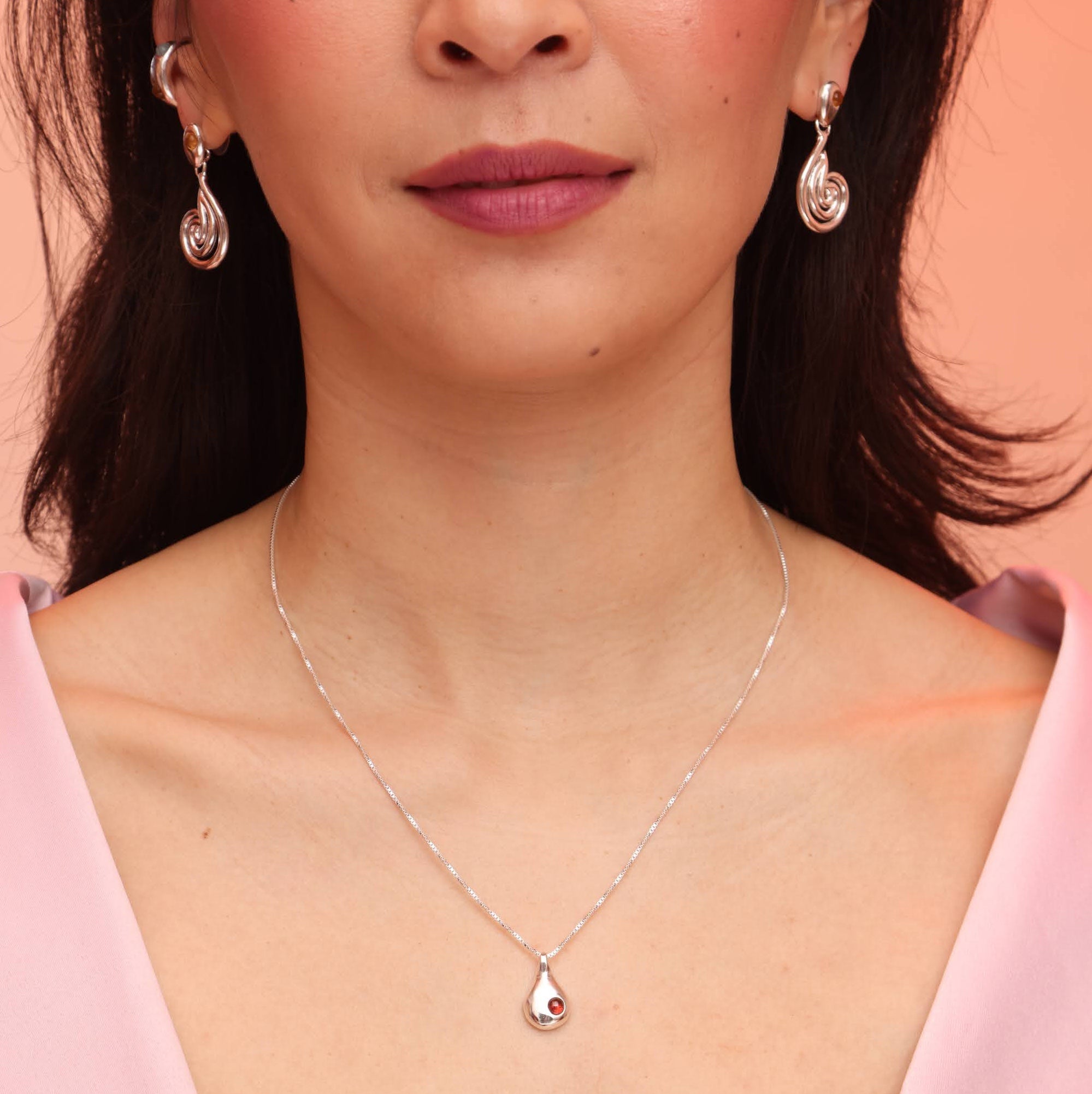 A person wearing a silver teardrop shaped necklace with a red garnet stone