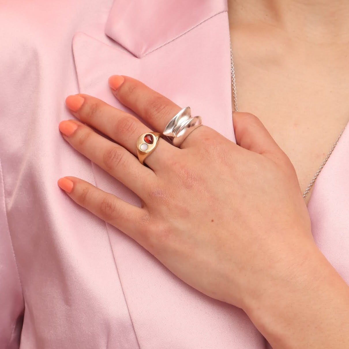A close up of a hand wearing three rings, two stacked silver rings with tall faces and one bronze round signet with two stones